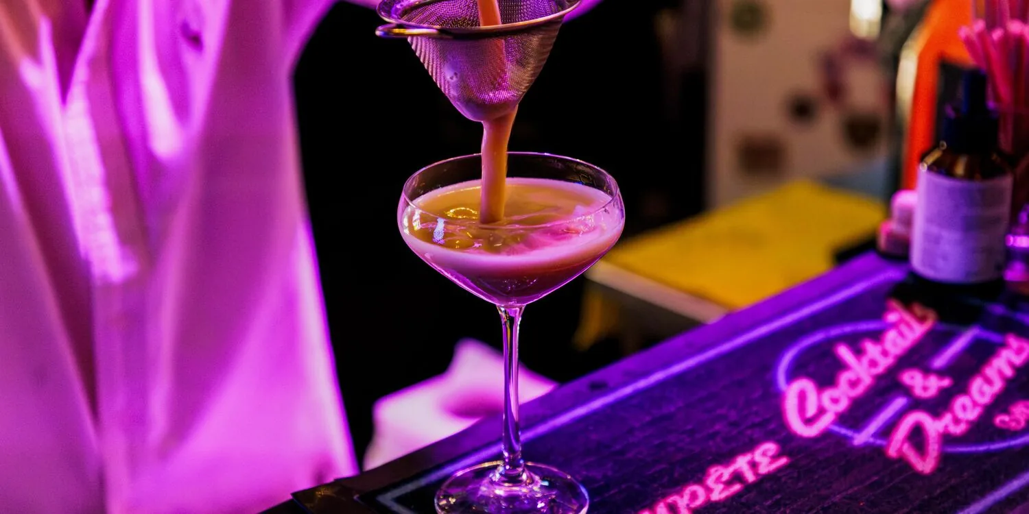 Un espresso martini versé devant l’enseigne lumineuse Cocktails & Dreams
